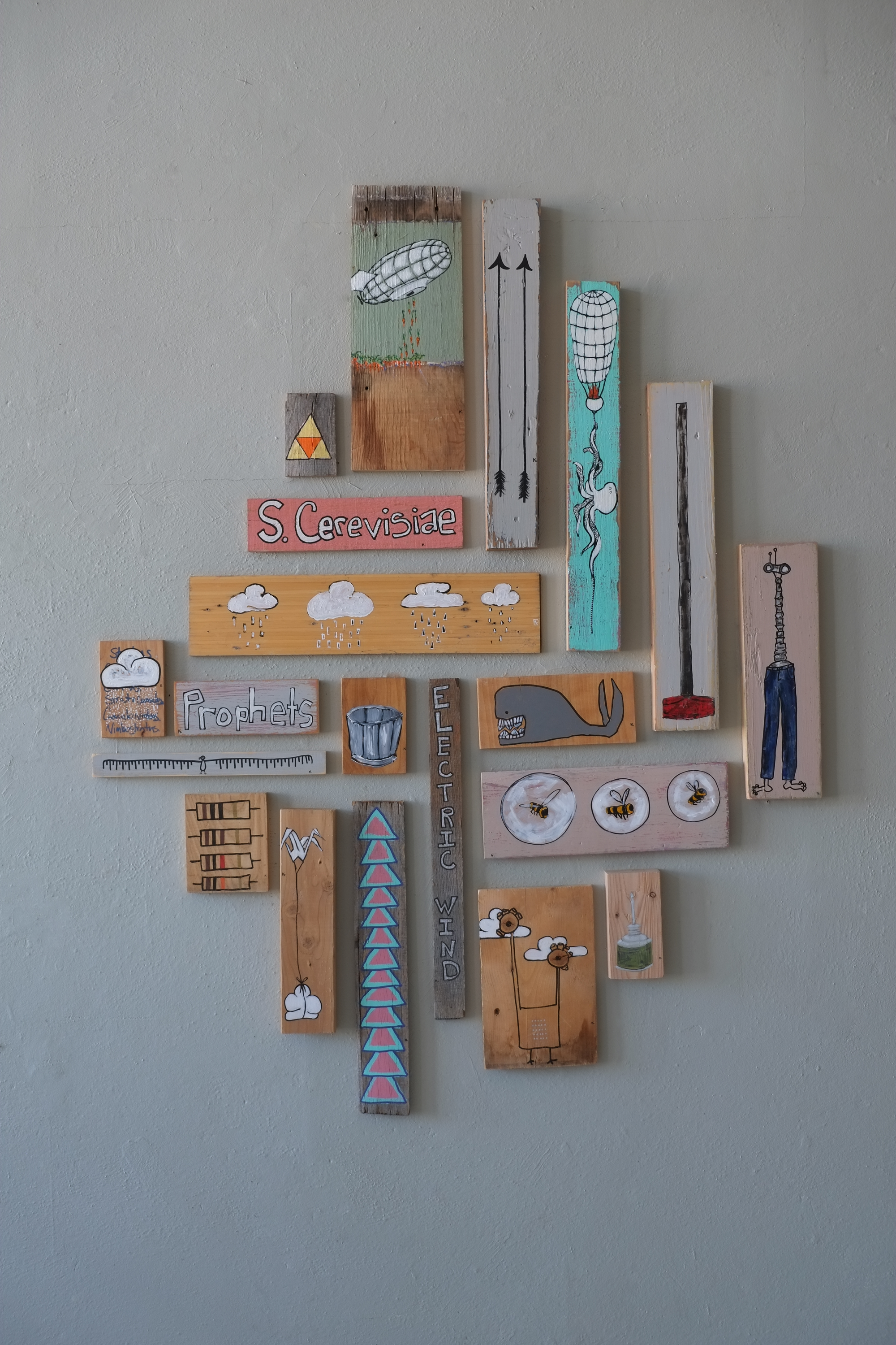 Site-specific installation of paintings on found wood panels, depicting figurative and symbolic imagery arranged as a group on a wall