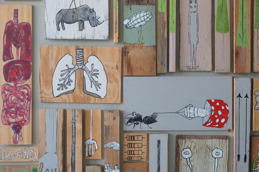 Gallery wall detail showing the painting alongside other works on found wood, including lungs, a rhino, and an airship piece.