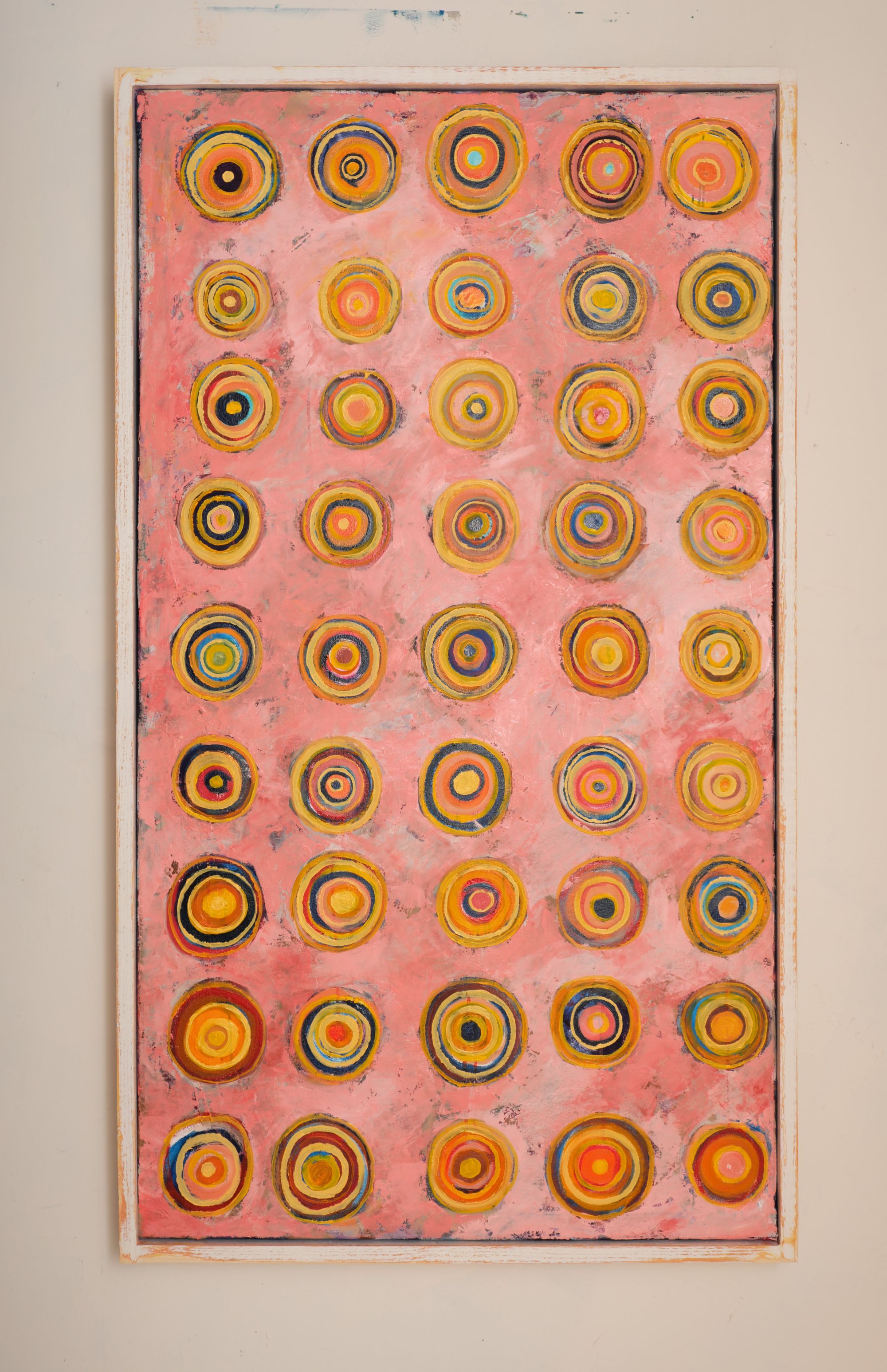 Oil painting featuring a grid of concentric circles in yellows, oranges, blues, and reds on a pink background, arranged in rows across a tall vertical composition.