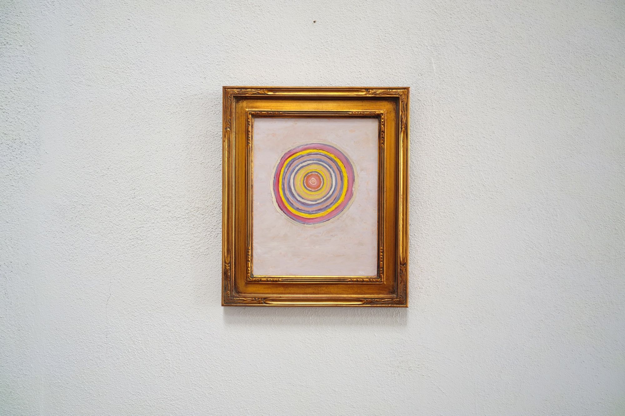 The painting Autumnal Twilight displayed on a white wall in its gold frame, showing the full composition of colorful concentric circles against the pale background from a gallery-distance perspective.