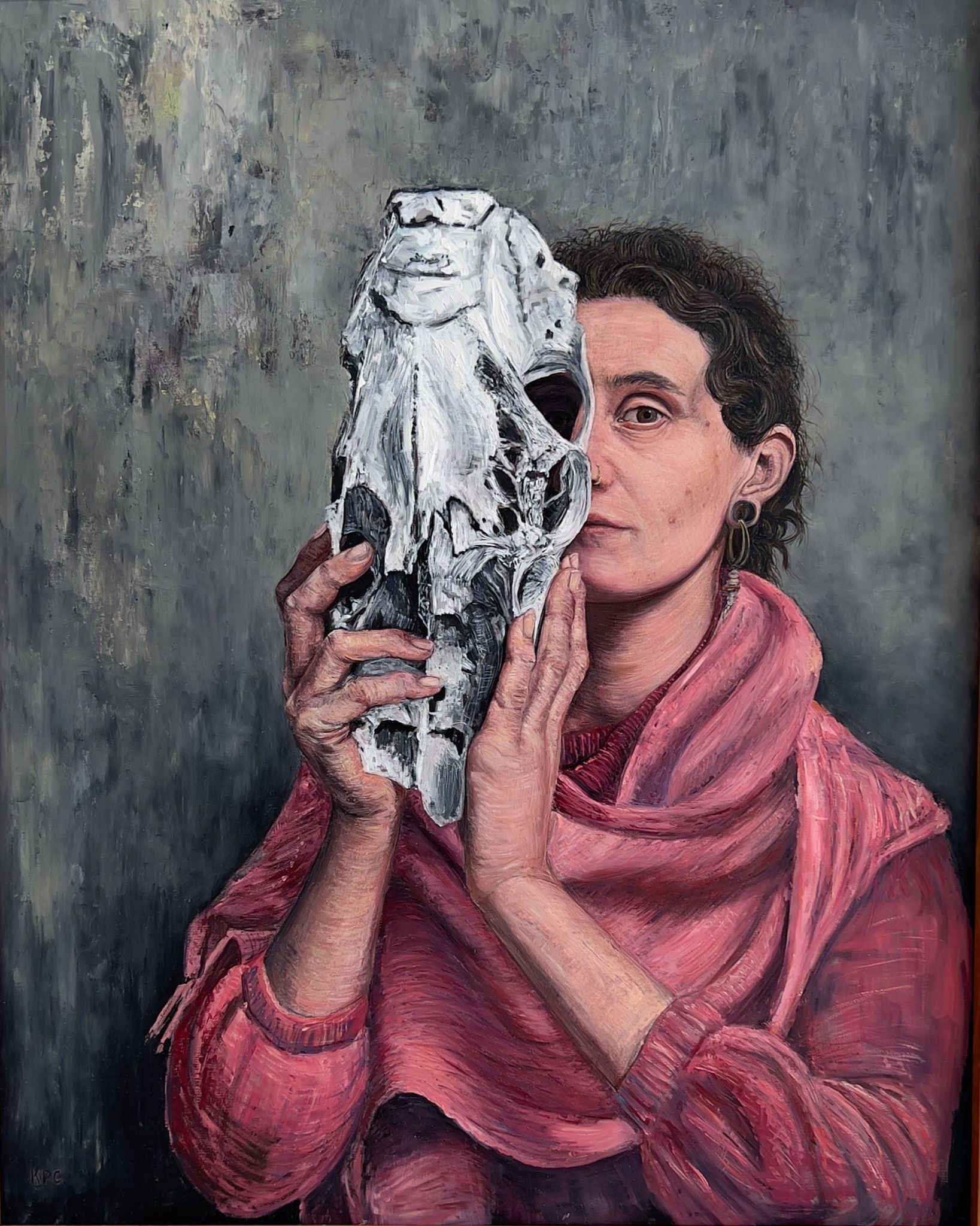Oil painting of a woman in a pink shawl holding a weathered white horse skull up to her face, partially obscuring it, against a muted gray-green textured background.