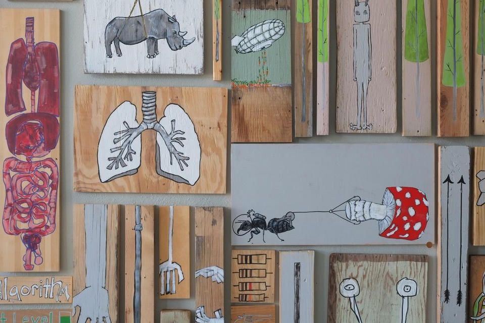 Gallery wall detail showing the painting alongside other works on found wood, including lungs, a rhino, and an airship piece.