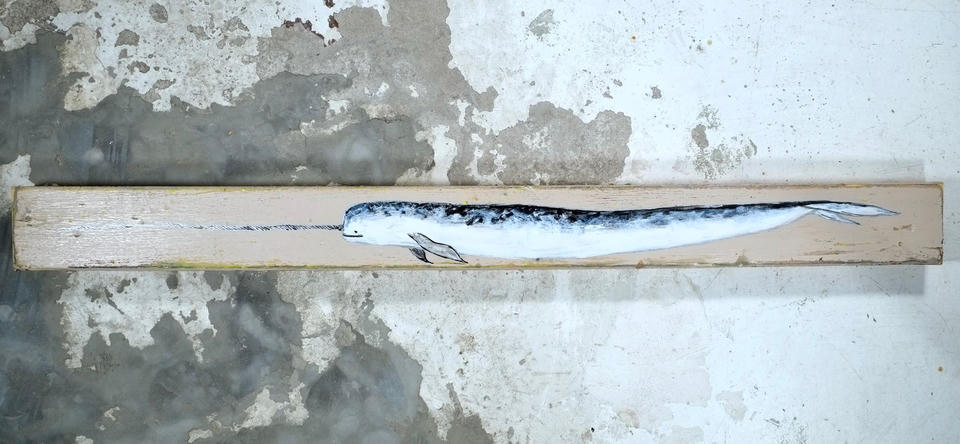 Acrylic painting on a long narrow piece of found wood depicting a narwhal in blue, black, and white with an extended spiral tusk, viewed from the side.