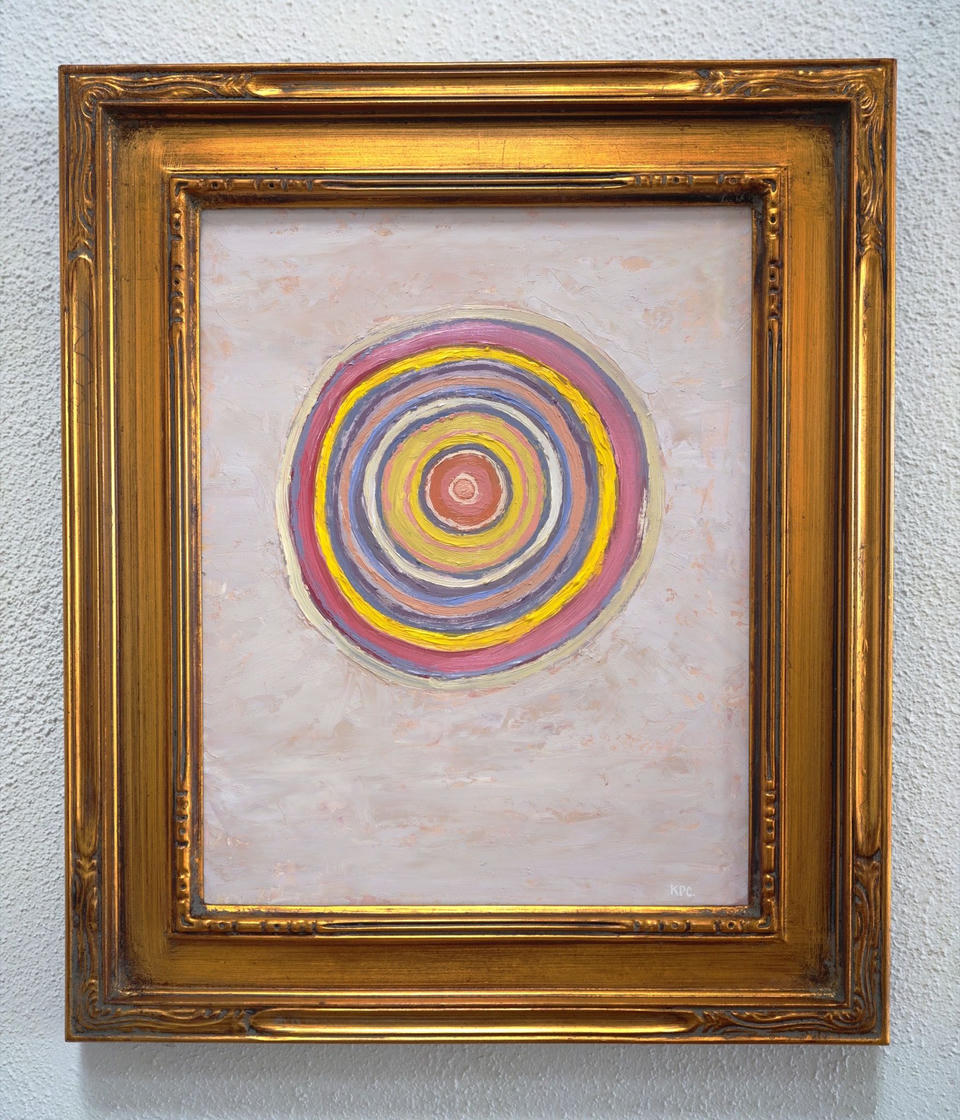 Close-up of the framed oil painting Autumnal Twilight in an ornate gold frame, showing concentric rings of pink, yellow, lavender, and white radiating from a coral center on a pale textured background.