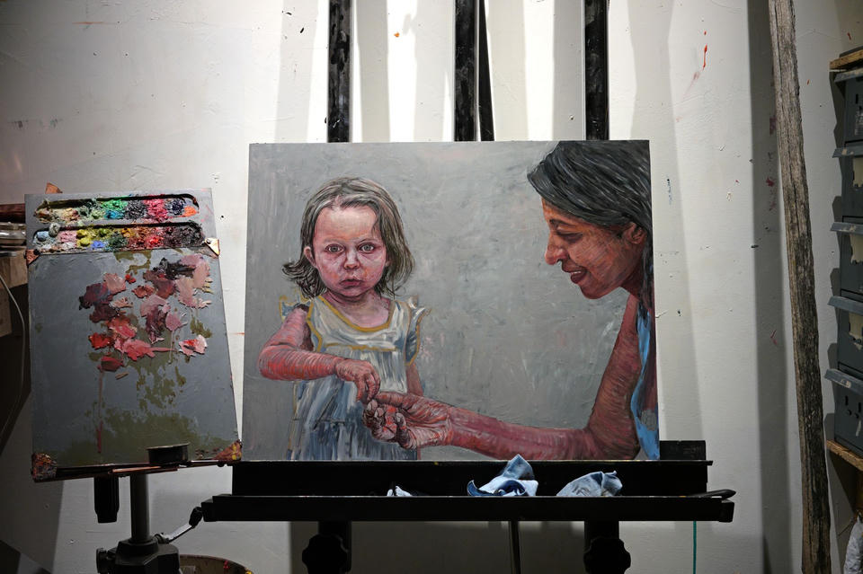 Oil painting in progress on an easel showing a young child in a white dress looking directly at the viewer while a woman beside her offers berries, rendered in expressive brushwork against a gray background.
