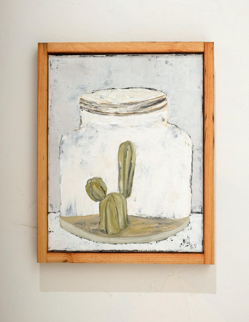 Oil painting of a small green saguaro cactus enclosed inside a large white glass jar with a lid, rendered with thick impasto brushwork against a pale gray-white background, in a wooden frame.