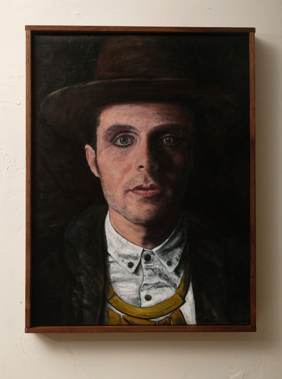 Oil on linen portrait of a young man in a dark hat, white button-up shirt, and yellow suspenders, dramatically lit against a black background.